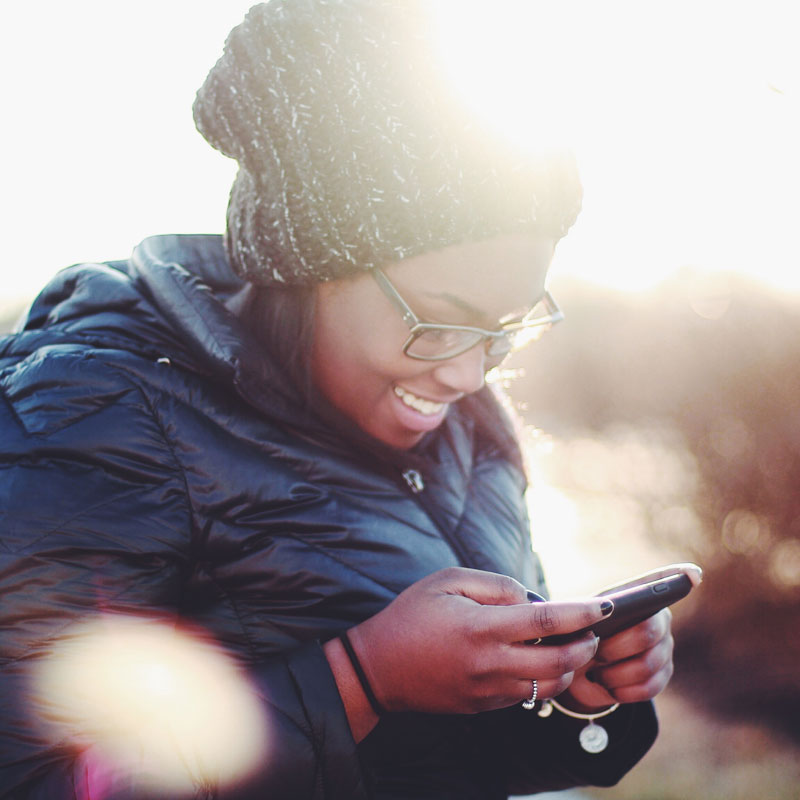 A woman in a winter coat and hat smiling at her phone